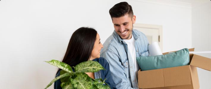 Couple with a plant and boxed items into a condo